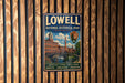 A vintage metal sign for Lowell National Historical Park, featuring an illustration of a building and a river, mounted on a wooden wall.