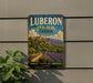 A vintage metal sign for Lubberon Park in France, featuring a scenic landscape with mountains, a village, and lavender fields.