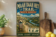 A vintage-style metal sign for the Maah Daha He Trail in North Dakota, featuring a scenic mountain landscape and trail marker.