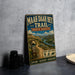 A vintage metal sign advertising the Maah Daha Hey Trail in North Dakota, featuring a scenic illustration of a trail surrounded by mountains and a river.