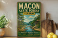 A vintage-style metal sign for the Macon State Forest in Alabama, featuring a scenic illustration of a river and forest landscape.