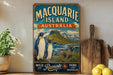 A vintage-style metal sign for Macquarie Island, Australia, featuring illustrations of penguins and a seal, with the text "Macquarie Island, Australia, Wild and Remote, Pure and Unspoiled".