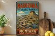 A vintage-style metal sign for Makoshika State Park in Montana, featuring a dinosaur skull and a mountain landscape.