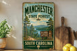 A vintage-style sign for Manchester State Forest in South Carolina, featuring a scenic landscape with pine trees, a lake, and mountains.