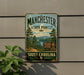 A vintage-style metal sign for Manchester State Forest in South Carolina, featuring a scenic landscape with pine trees, a lake, and mountains.