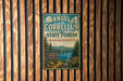 A vintage metal sign for the Manuel F. Correllus State Forest in Massachusetts, featuring a scenic landscape with pine trees, a lake, and mountains.