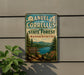 A vintage metal sign for the Manuel Correllus State Forest in Massachusetts, featuring a scenic landscape with pine trees, a river, and mountains.