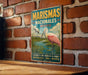 A vintage-style metal sign with a pink flamingo and text in Spanish, mounted on a brick wall.