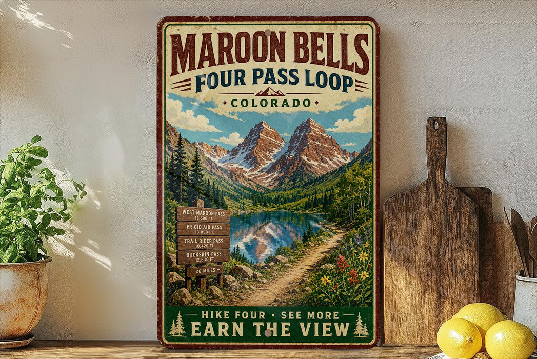 A vintage-style metal sign advertising the Maroon Bells Four Pass Loop in Colorado, featuring a scenic mountain landscape with a lake and trail.
