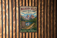 A vintage-style metal sign for Maroon Bells Four Pass Loop in Colorado, featuring a mountain landscape with a lake and trail.