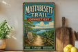 A vintage-style metal sign for the Mattabesett Trail in Connecticut, featuring a scenic landscape with a path leading through a forest and a lake.