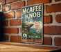 A vintage-style metal sign for the Mcafee Knob Trail in Virginia, featuring a scenic mountain landscape and the trail's name.