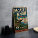 A vintage-style metal sign for the Mcafee Knob Trail, featuring a scenic mountain landscape and the text "Take in the View! Keep it Wild!" The sign is displayed on a gray concrete surface, with a stack of black camera lenses and a white dish visible in the background.