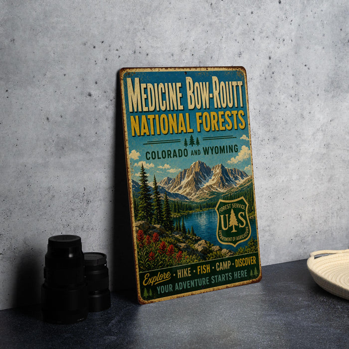 a vintage-style metal sign advertising the Medicine Bow-Rout National Forests in Colorado and Wyoming, with a mountain landscape and a river in the background.