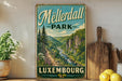A vintage metal sign for Meisterdall Park in Luxembourg, featuring a scenic mountain landscape with a winding river.