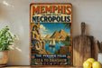 A vintage-style poster advertising "Memphis and its Necropolis" featuring the pyramids of Giza, with a wooden board and a potted plant in the foreground.