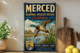 A vintage-style sign for the Merced National Wildlife Refuge in California, featuring a duck in flight and a scenic landscape.
