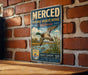 A vintage-style metal sign for the Merced National Wildlife Refuge in California, featuring a duck in flight and a serene landscape.