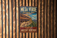 A vintage-style metal sign for the Mesa Verde National Park in the United States, featuring a scenic image of the ancient cliff dwellings.