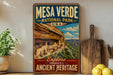 A vintage-style metal sign for the Mesa Verde National Park in the United States, featuring a scenic image of the ancient cliff dwellings in the background.