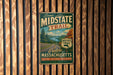 A vintage metal sign for the "Scenic Midstate Trail" in Massachusetts, featuring a scenic landscape with a road and trees.