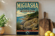A vintage-style metal sign for the Miguasha National Park in Canada, featuring a scenic landscape with a rocky coastline, pine trees, and a large rock formation.