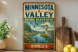 A vintage-style sign for the Minnesota Valley National Wildlife Refuge, featuring an illustration of a bird, a river, and a landscape with trees and flowers.