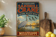 A vintage-style sign for the Mississippi Sandhill Crane National Wildlife Refuge, featuring an illustration of a crane standing in a grassy field with a sunset in the background.