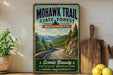 a vintage-style sign for the Mohawk Trail in Massachusetts, with a scenic mountain landscape and a winding road. The sign is displayed on a wooden shelf, surrounded by various kitchen utensils and a potted plant.