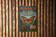 A vintage-style metal sign with a butterfly illustration, mounted on a wooden wall.