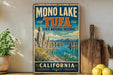 A vintage-style metal sign for the Mono Lake Tufa State Natural Reserve in California, featuring a scenic landscape with mountains, water, and a wooden paddle.