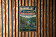 A vintage-style metal sign for Monongahela River Valley Heritage Corridor, featuring a scenic image of a river and a steamboat, is displayed on a wooden wall.