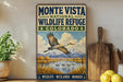 A vintage-style sign for the Monte Vista National Wildlife Refuge in Colorado, featuring a bird in flight over a scenic landscape with mountains and a lake.