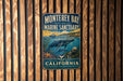 A vintage metal sign for Monterey Bay National Marine Sanctuary, featuring an illustration of marine life and the text "California" and "Explore & Protect"