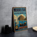 A vintage metal sign for Morro Bay State Marine Recreational Management Area, featuring a sailboat and sea lions, is displayed on a gray concrete surface.