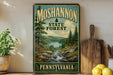 A vintage-style metal sign for the Moshannon State Forest in Pennsylvania, featuring a scenic landscape with a river and pine trees.