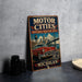 A vintage-style metal sign advertising the Motor Cities National Heritage Area in Michigan, featuring an illustration of a classic red car and a bridge.