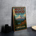 A vintage-style metal sign for Mount Hood National Forest in Oregon, featuring a mountain landscape with pine trees and a river.