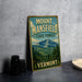 A vintage-style sign for Mount Mansfield State Forest in Vermont, featuring a mountain landscape and pine trees.