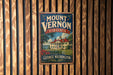 A vintage-style sign for Mount Vernon, Virginia, featuring a house and trees, mounted on a wooden wall.