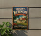 A vintage-style sign for Mount Vernon, Virginia, featuring a house and trees, mounted on a wall next to a plant.
