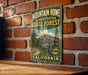 A vintage-style metal sign for the Mountain Home State Forest in California, featuring a scenic mountain landscape and pine trees.