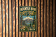 A vintage metal sign for the Mountain Home State Forest in California, featuring a scenic mountain landscape and pine trees.