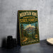 A vintage-style metal sign for the Mountain Home State Forest in California, featuring a scenic mountain landscape and a bear symbol.