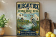 A vintage-style metal sign for Muscatuck National Wildlife Refuge in Indiana, featuring an illustration of a heron and ducks in a pond surrounded by reeds and a wooden structure.