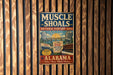 A vintage metal sign advertising the Muscle Shoals National Heritage Area in Alabama, featuring a microphone, a piano, and a sign for the Hit Recording Capital.