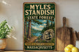 A vintage-style metal sign for the Myles Standish State Forest in Massachusetts, featuring a scenic illustration of a forest and a river.