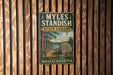 A vintage metal sign for Myles Standish State Forest in Plymouth County, Massachusetts, featuring a scenic illustration of a forest and a lake.
