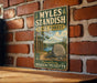 A vintage-style metal sign for the Myles Standish State Forest in Plymouth, Massachusetts, mounted on a brick wall.