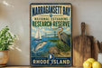 A vintage-style metal sign for Narragansett Bay National Estuarine Research Reserve, featuring illustrations of a sailboat, a heron, and a bridge.